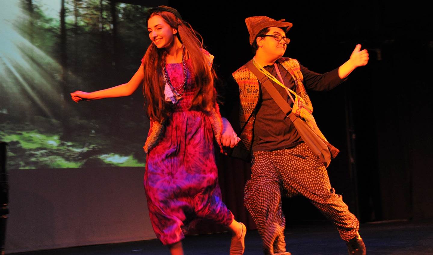 A young woman and boy are holding hands smiling as hey walk across the stage.