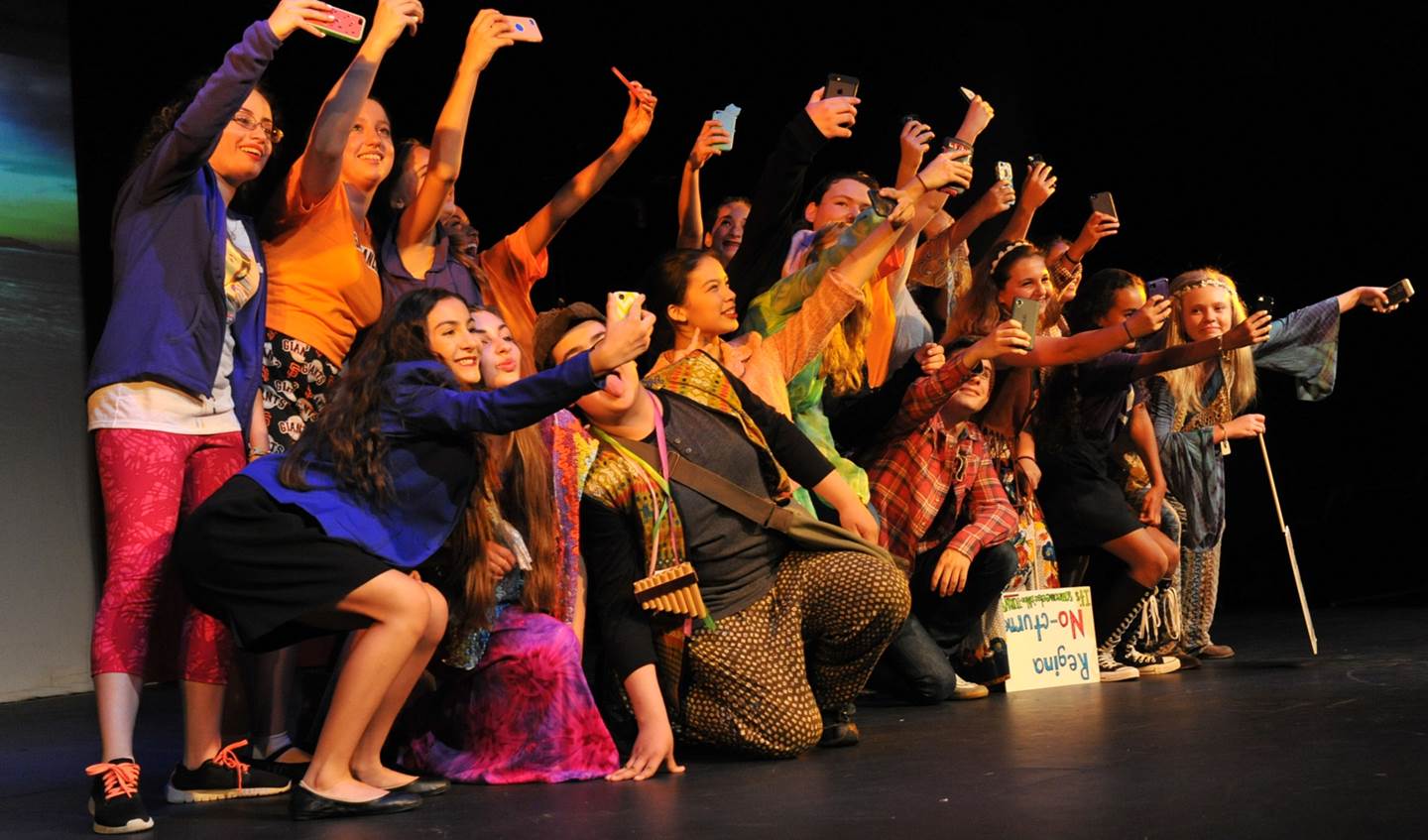 A group of students on stage all taking selfies of themselves.