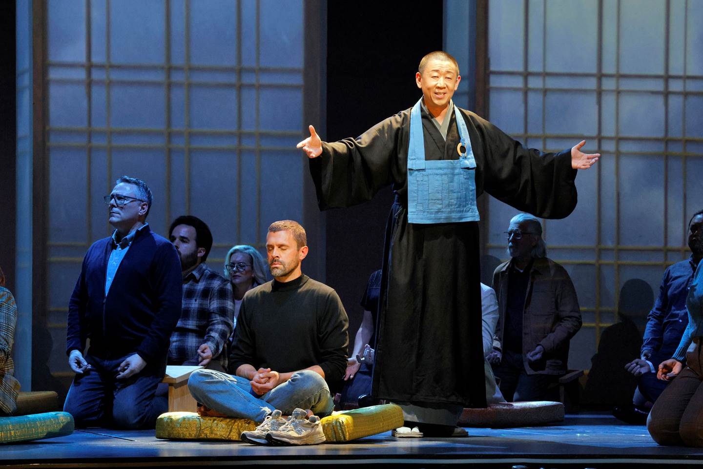 several people sitting cross-legged or kneeling on pads with a guru having his arms outstretched