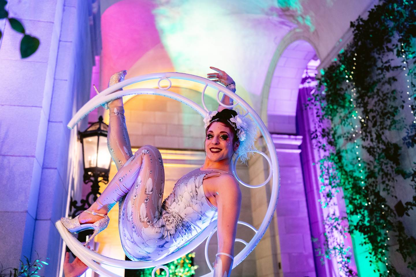 A female performer in a white bodysuit perched inside a crescent moon.